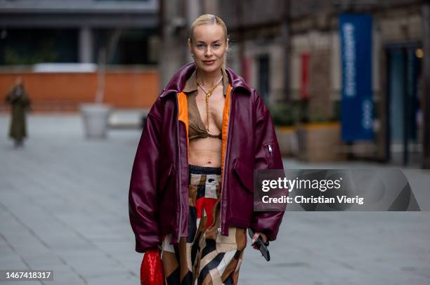 Thora Valdimars wears cropped top, burgundy oversized bomber jacket, pants with print, red Bottega Veneta bag outside Eudon Choi during London...