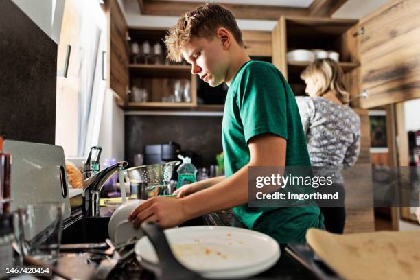 teenage boy washing the dishes after the lunch - wash the dishes stockfoto's en -beelden