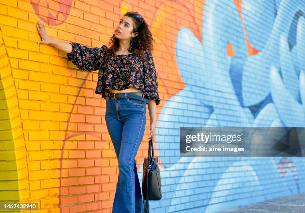 side view of a beautiful woman standing in casual clothes touching a wall with smiling graffiti - graffiti hintergrund stock pictures, royalty-free photos & images