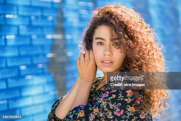 frontal view of beautiful latina woman standing looking at the camera while adjusting an earring with graffiti in the background. - portrait frontal stock pictures, royalty-free photos & images