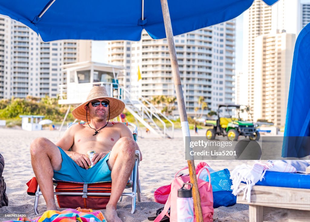 Happy fit guy in his 40’s hanging out on an idyllic beach vacation on a beach chair with sun hat