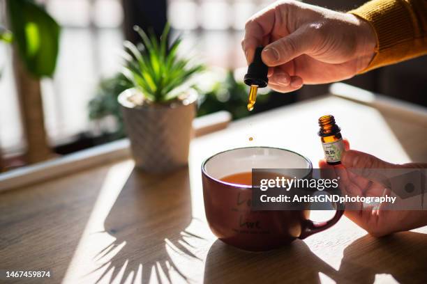 hombre usando aceite de cbd en su té. - homeopatía fotografías e imágenes de stock