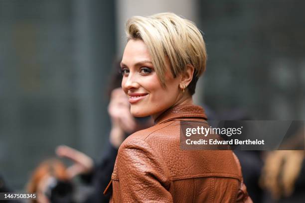 Wallis Day wears gold earrings, a camel shiny leather long coat , outside David Koma, during London Fashion Week February 2023 on February 18, 2023...