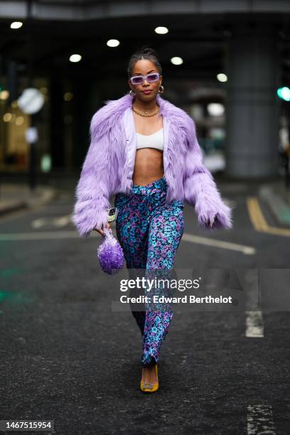 Ellie Delphine wears pale purple square sunglasses, gold earrings, gold necklace, a white V-neck / cropped top, a pale purple fluffy fur jacket,...