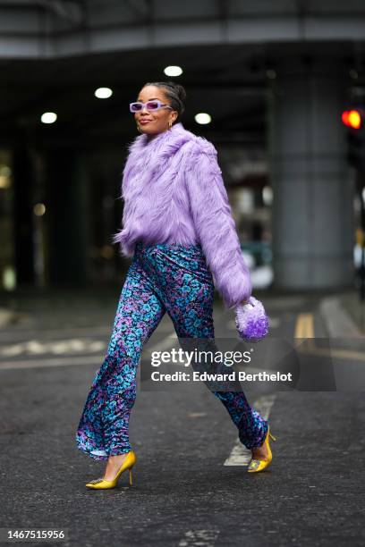 Ellie Delphine wears pale purple square sunglasses, gold earrings, gold necklace, a white V-neck / cropped top, a pale purple fluffy fur jacket,...