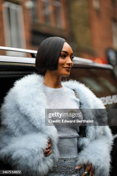 Jourdan Dunn wears silver small earrings, a pale blue oversized fluffy fur jacket, a pale blue wool halter neck t-shirt, a pale blue silk / satin...