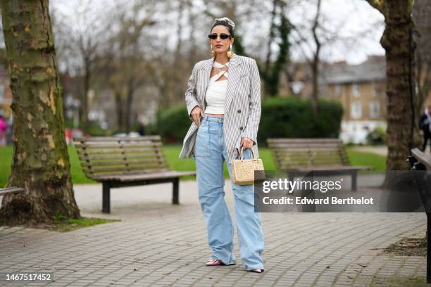 Bettina Looney wears a beige ribbed wool hair elastic, black sunglasses, a white large stones and pendant gold earrings, a gold chain pendant...