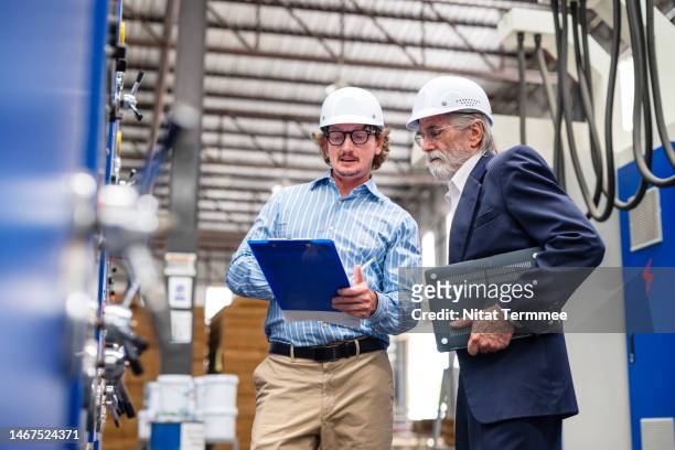 identifying and managing business risks in manufacturing operations. businessmen discuss plans and strategies over reports data in front of machinery to identify which risks pose to their operations on the production line factory floor. - business process stock-fotos und bilder