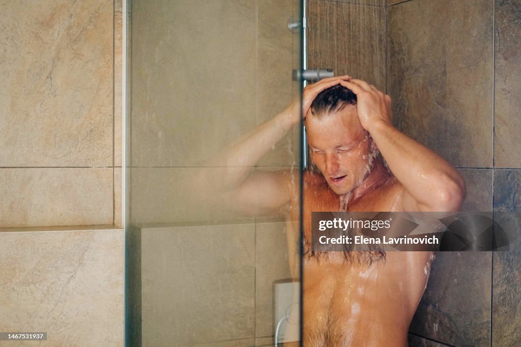 Photo of a man in the shower. Real man washing his hair in the shower at home