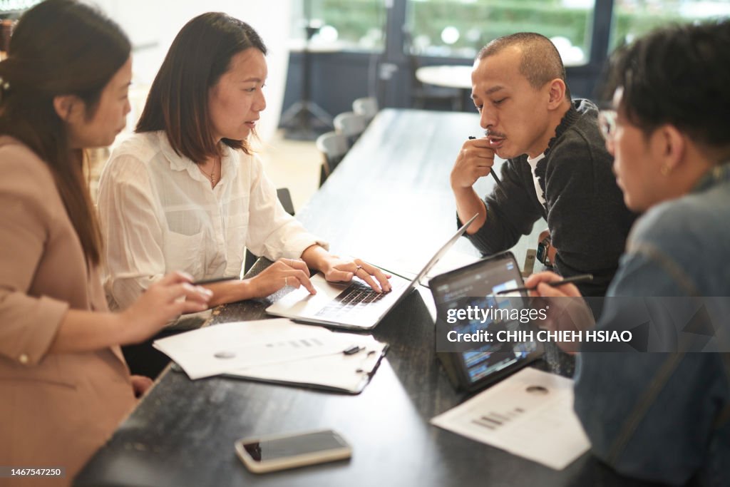Young Asian coworkers discussing business strategy in a coffee shop.