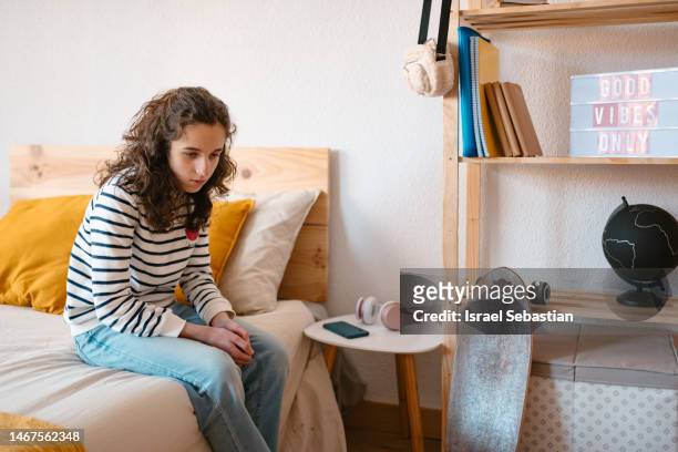 view of a teenage girl sitting on the edge of the bed with a sad face. - alpha female stock pictures, royalty-free photos & images