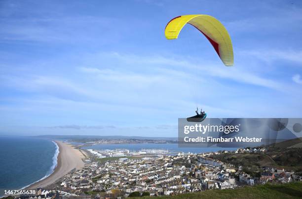 Paraglider enjoys the weather as they fly over Chesil beach in Dorset, on February 19, 2023 in Portland, England.