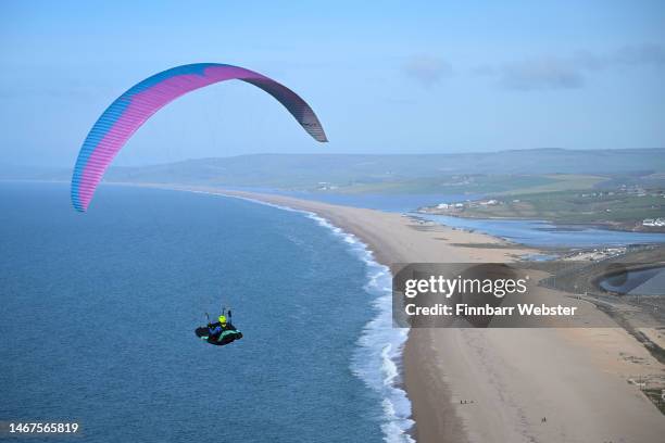 Paraglider enjoys the weather as they fly over Chesil beach in Dorset, on February 19, 2023 in Portland, England.