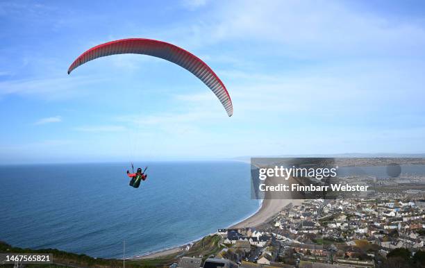 Paraglider enjoys the weather as they fly over Chesil beach in Dorset, on February 19, 2023 in Portland, England.