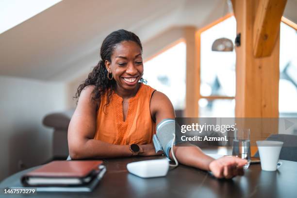 black female in 40s using a medical device for measuring blood pressure - blood pressure gauge stock pictures, royalty-free photos & images