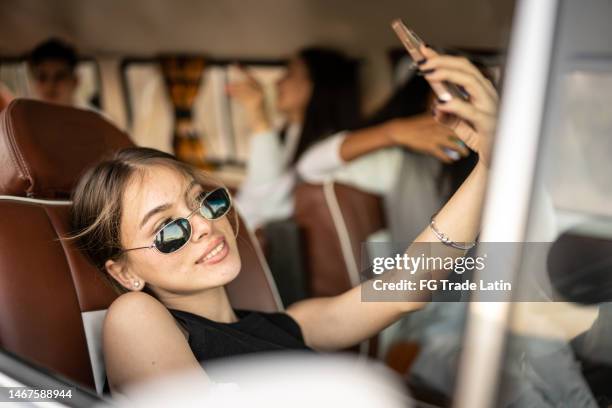 mujer joven tomando selfie o filmando sentada en el asiento del pasajero en el transporte retro mini van - influencer fotografías e imágenes de stock