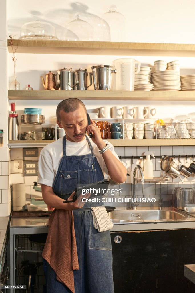 Photo of Asia cafe owner in coffee shop answer a call and hold a wireless digital tablet order products online.