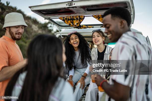 group of young friends drinking soda and talking on the trunk of a van outdoors - drinking soda in car stock pictures, royalty-free photos & images