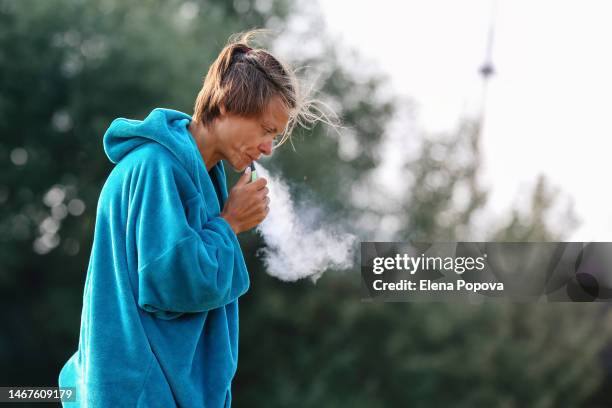 mid adult female surfer wearing warm hoodie bathrobe smoking electronic cigarette at the river shore - unhealthy living bildbanksfoton och bilder