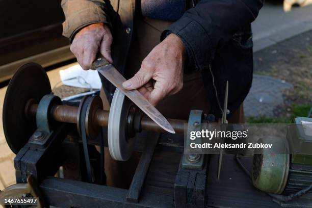 an elderly man sharpens a knife on a grinding wheel at a street market in batumi, georgia. an old man is holding a knife. a simple life in the countryside. a poor pensioner earns money by providing knife grinder services at the local market. - sharpening stock-fotos und bilder