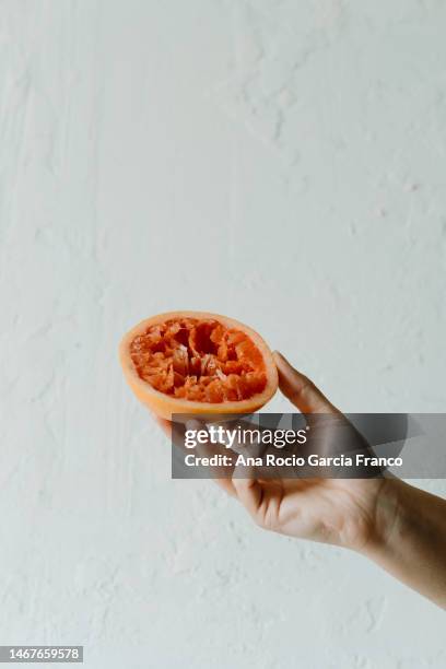 hand holding a squeezed grapefruit - orange squeeze on white stock-fotos und bilder