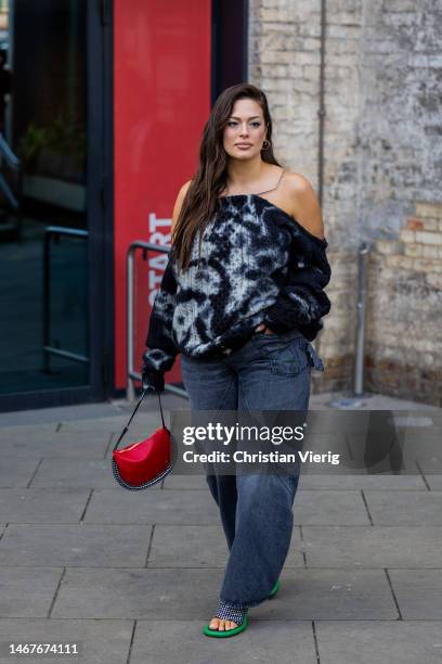 Ashley Graham wears blue off shoulder jumper, red bag, denim skirt outside JW Anderson during London Fashion Week February 2023 on February 19, 2023...