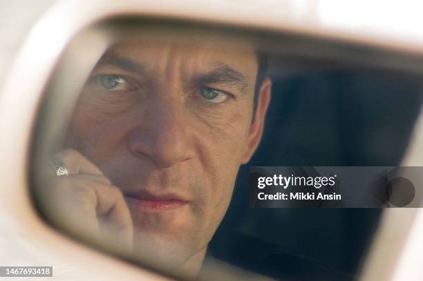 View of English actor Jason Isaacs reflected in the side mirror of a car during the filming of an episode of the cable television series...