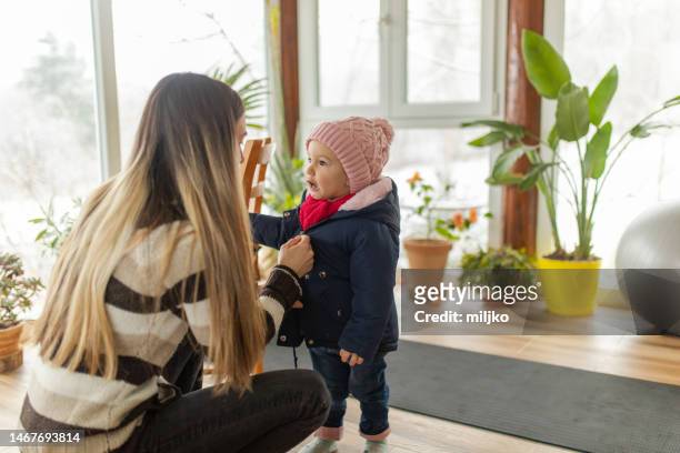 mutter und ihre tochter bereiten sich darauf vor, im winter nach draußen zu gehen - baby mütze anziehen stock-fotos und bilder