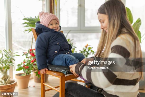 mutter und ihre tochter bereiten sich darauf vor, im winter nach draußen zu gehen - baby mütze anziehen stock-fotos und bilder