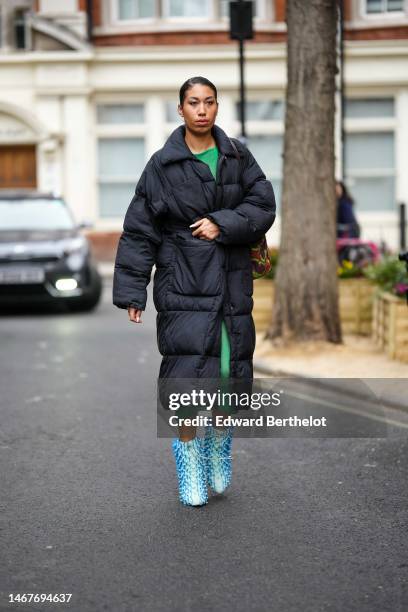 Guest wears a gold chain necklace, a green wool long dress, a black long puffer jacket, a burgundy / green / red print pattern shoulder bag, flashy...