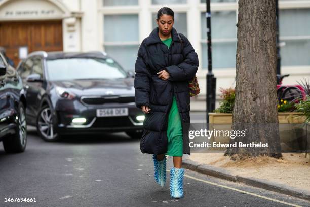 Guest wears a gold chain necklace, a green wool long dress, a black long puffer jacket, a burgundy / green / red print pattern shoulder bag, flashy...