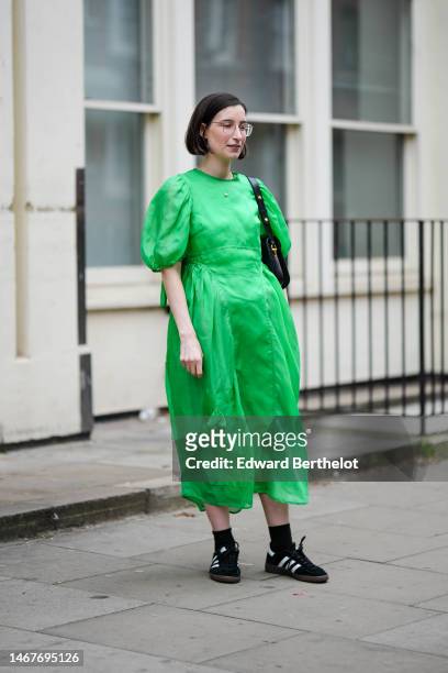Guest wears gold glasses, a green short puffy sleeves / long midi dress, a black shiny leather with a gold horse bite buckle shoulder bag, black...