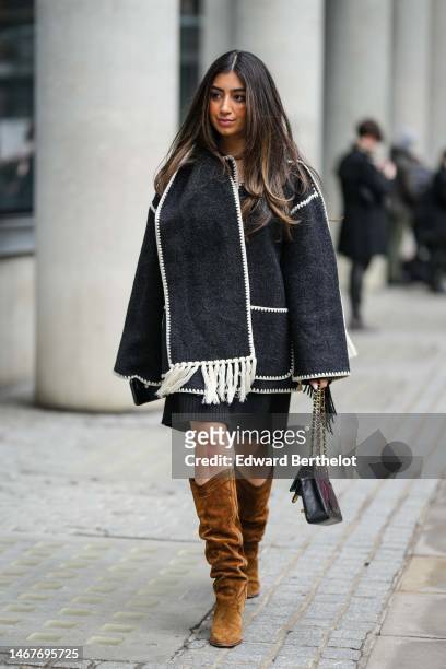 Guest wears a dark gray wool with white latte fringed borders oversized coat, a black wool short dress, a black shiny leather Timeless handbag from...