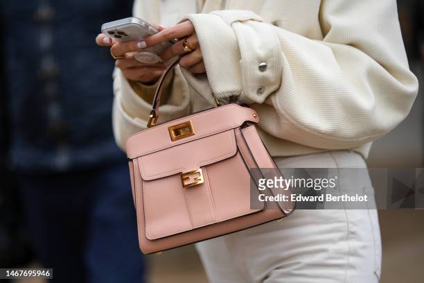 Guest wears a white latte ribbed velvet zipper jacket, a pale pink matte leather handbag from Fendi, white denim pants, gold necklaces, outside...