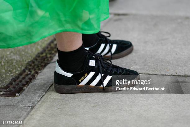 Guest wears a green short puffy sleeves / long midi dress, black socks, black suede with white leather logo sneakers from Adidas, outside...
