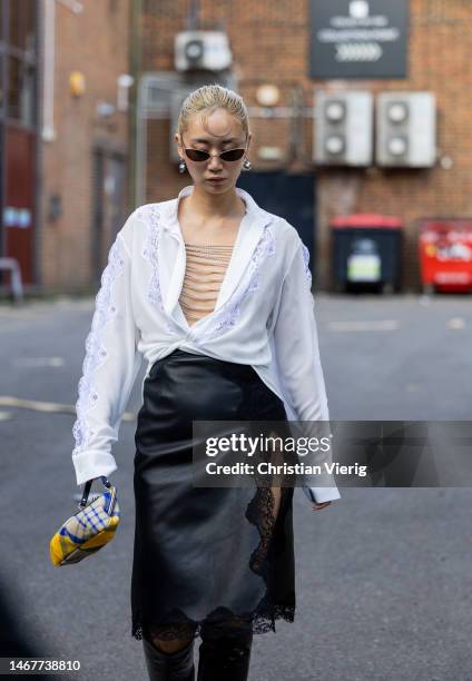 Betty Bachz wears white blouse, black laced leather skirt with slit, bag, knee high boots outside Christopher Kane during London Fashion Week...