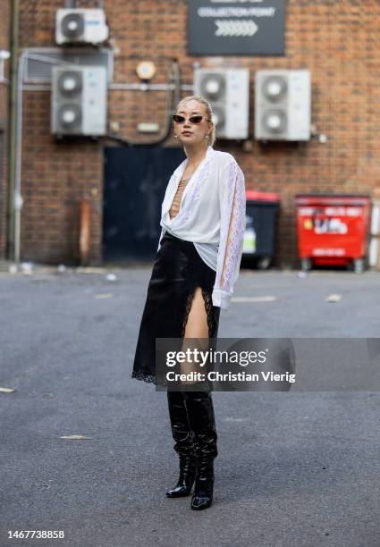 Betty Bachz wears white blouse, black laced leather skirt with slit, bag, knee high boots outside Christopher Kane during London Fashion Week...