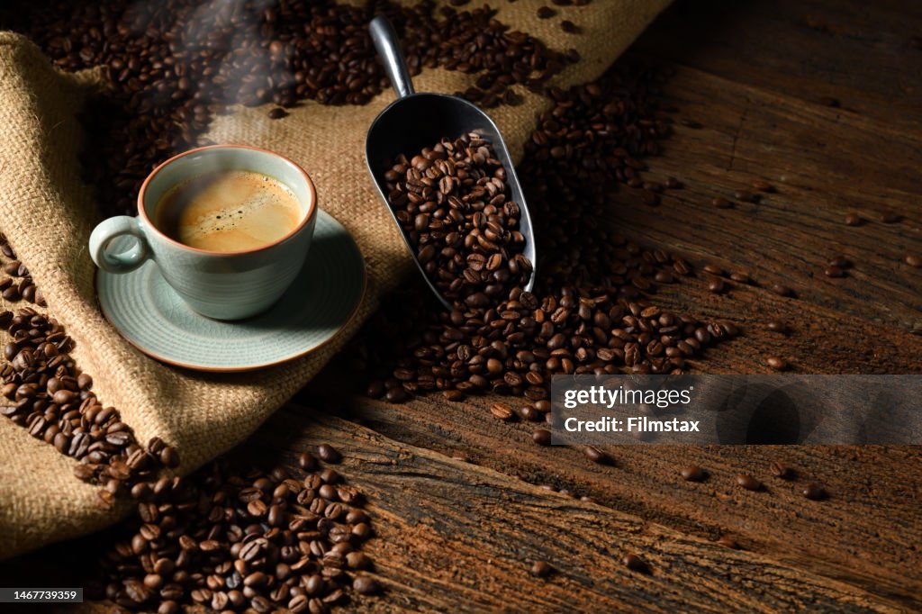 Cup of coffee with smoke and coffee beans on old wooden background