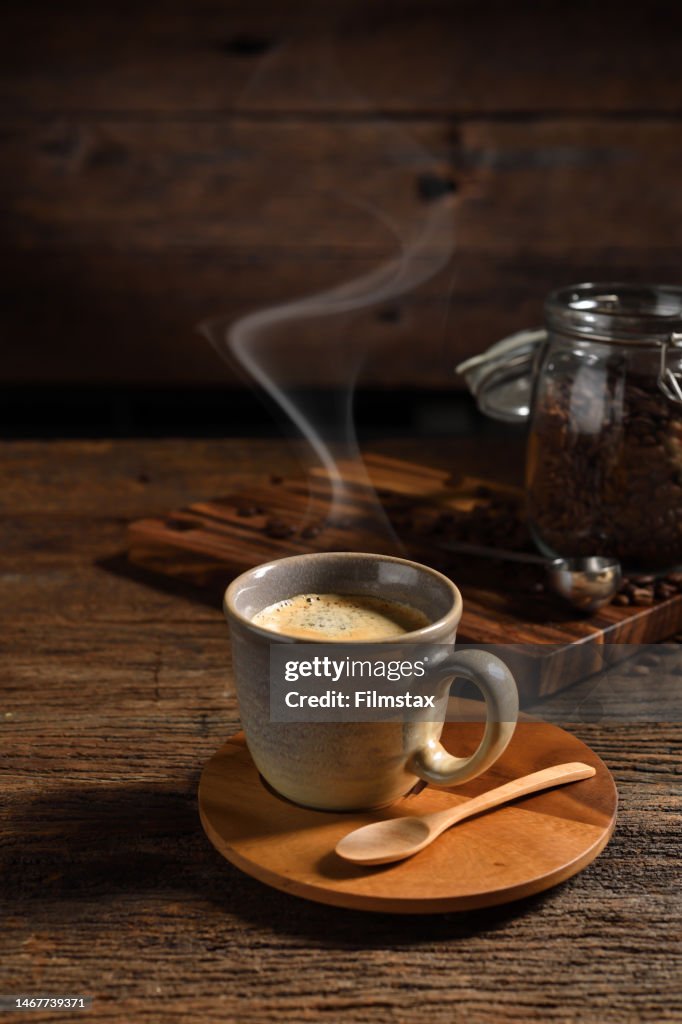 Cup of coffee with smoke and coffee beans on old wooden background