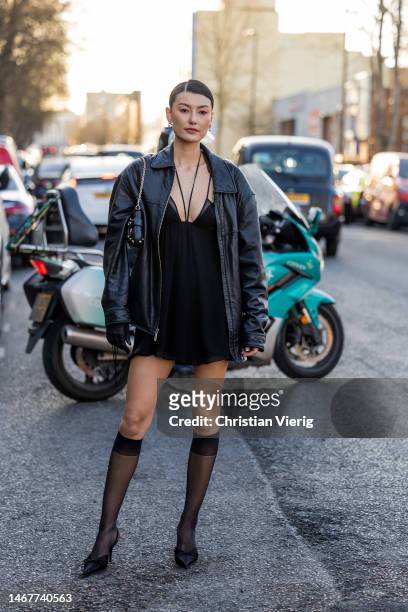 Amalie Gassmann wears black leather jacket, dress, knee high transparent socks, heels, bag outside Nensi Dojaka during London Fashion Week February...