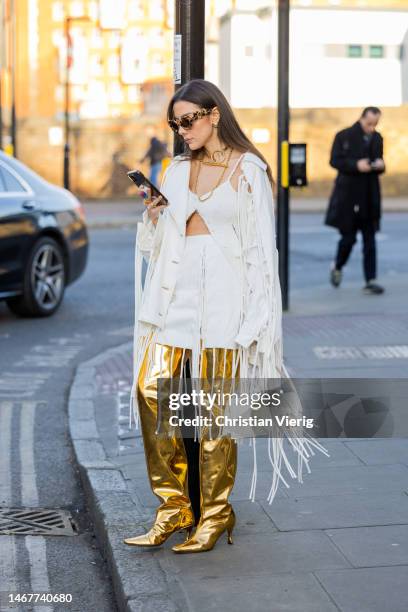 Mina Habchi wears golden over knees boots, white skirt, top, jacket with fringes, Jacquemus bag, sunglasses outside Nensi Dojaka during London...