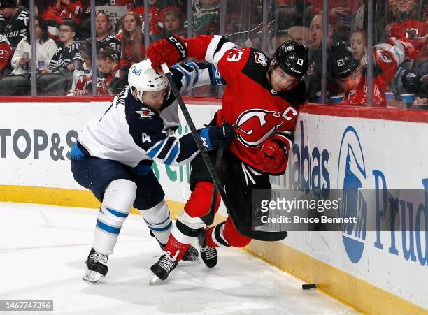 Neal Pionk of the Winnipeg Jets checks Nico Hischier of the New Jersey Devils into the boards during the second period at the Prudential Center on...
