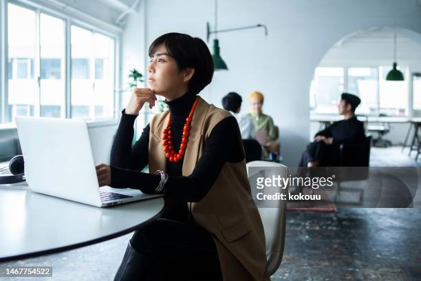 businesswoman using laptop in the office and other colleagues on background - woman thinking stock pictures, royalty-free photos & images