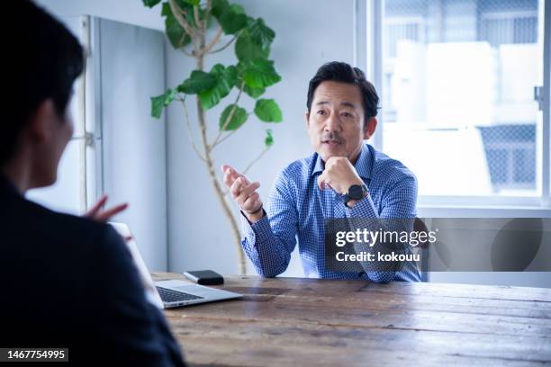 机の向かいに座っている若い男に助言する中年男性 - ビジネスフォーマル ストックフォトと画像