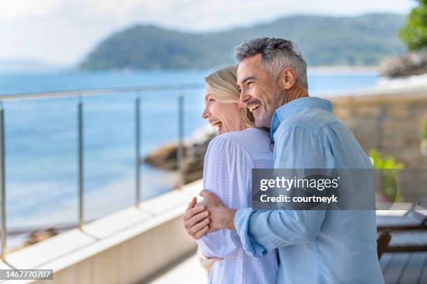 pareja madura abrazada en un balcón frente al mar. - pareja madura fotografías e imágenes de stock
