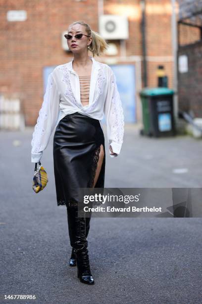 Betty Bachz wears black sunglasses, silver earrings, a white lace print pattern with V-neck with embroidered silver chains blouse, a black shiny...