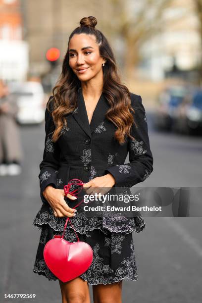 Tamara Kalinic wears micro earrings, a black with embroidered white flower pattern V-neck / long sleeves / ruffled short dress, a red shiny leather...