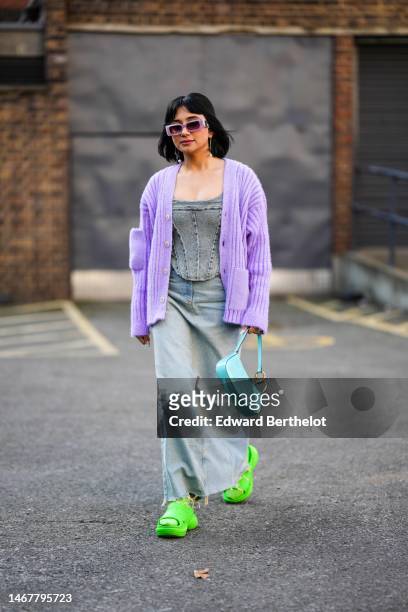 Guest wears pale purple sunglasses, gold pendant earrings from Valentino, a blue and gray denim shoulder-off / corset top, a pale purple ribbed wool...
