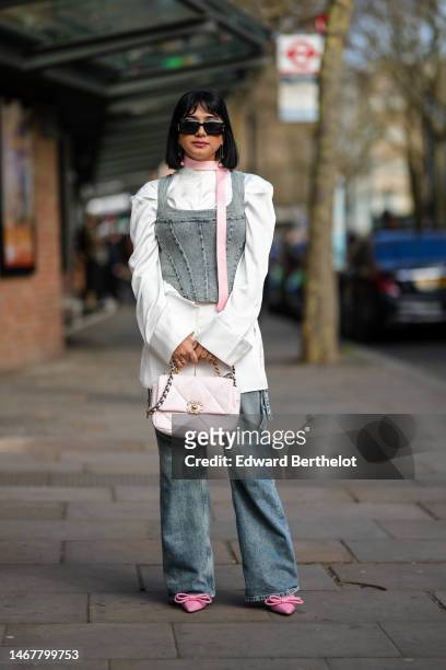 Guest wears black sunglasses, a pale pink small scarf, a white oversized shirt, a pale gray denim corset tank-top, a pale pink shiny leather Chanel...