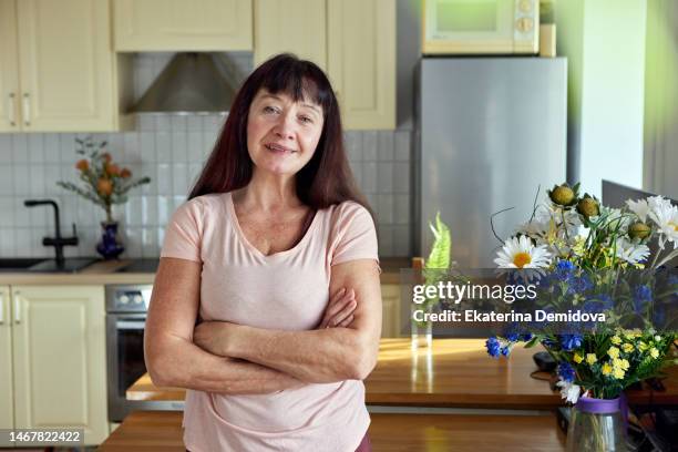 elderly woman in the kitchen smiling looking at camera arms crossed on chest - woman flat chest 個照片及圖片檔